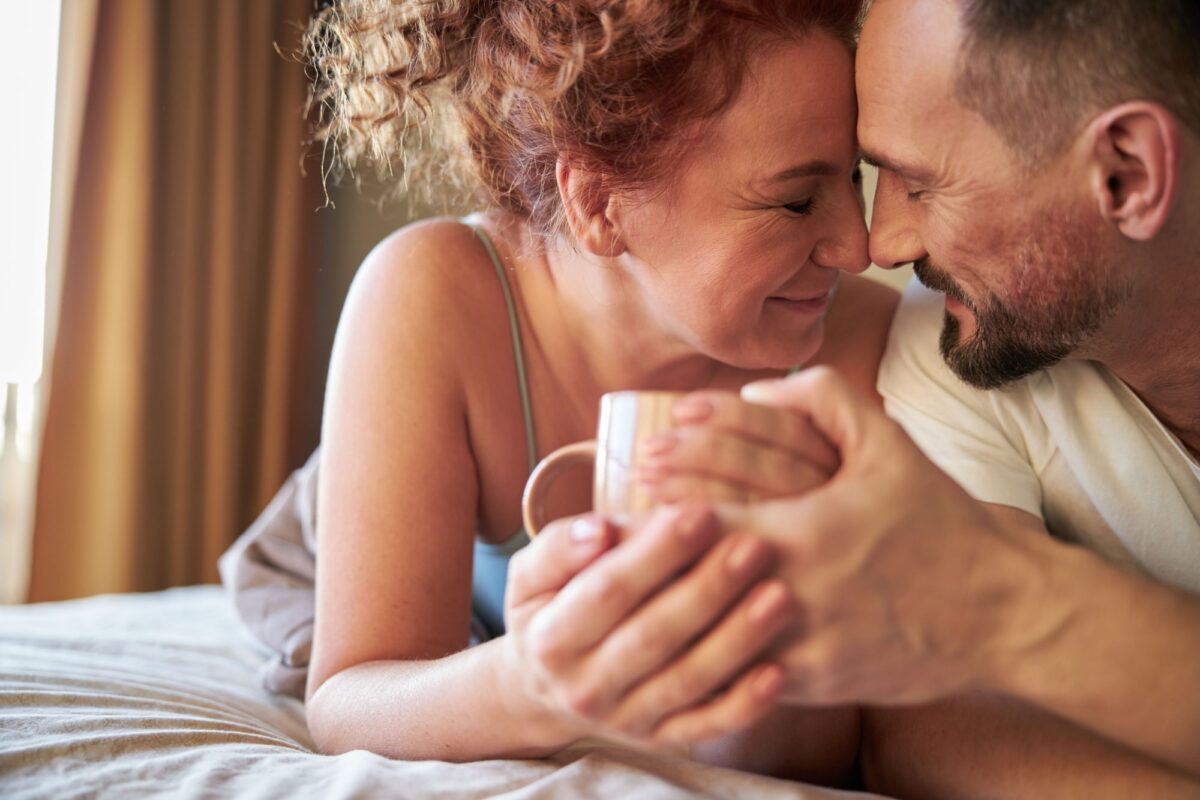 smiling lovely couple with coffee lying in bed